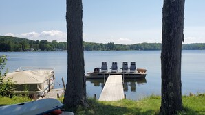 Une jetée avec des bateaux et des chaises, entourée d’arbres et bordant un lac paisible.