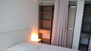 Ein Hotelzimmer mit einem Bett, einem Nachttisch mit Lampe, einem Kleiderschrank und einem Regal mit Lampe.