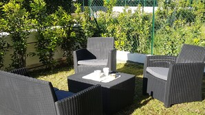 Ein Gartenmöbel-Set aus Rattan mit Tisch und Stühlen, umgeben von Gras und Pflanzen.
