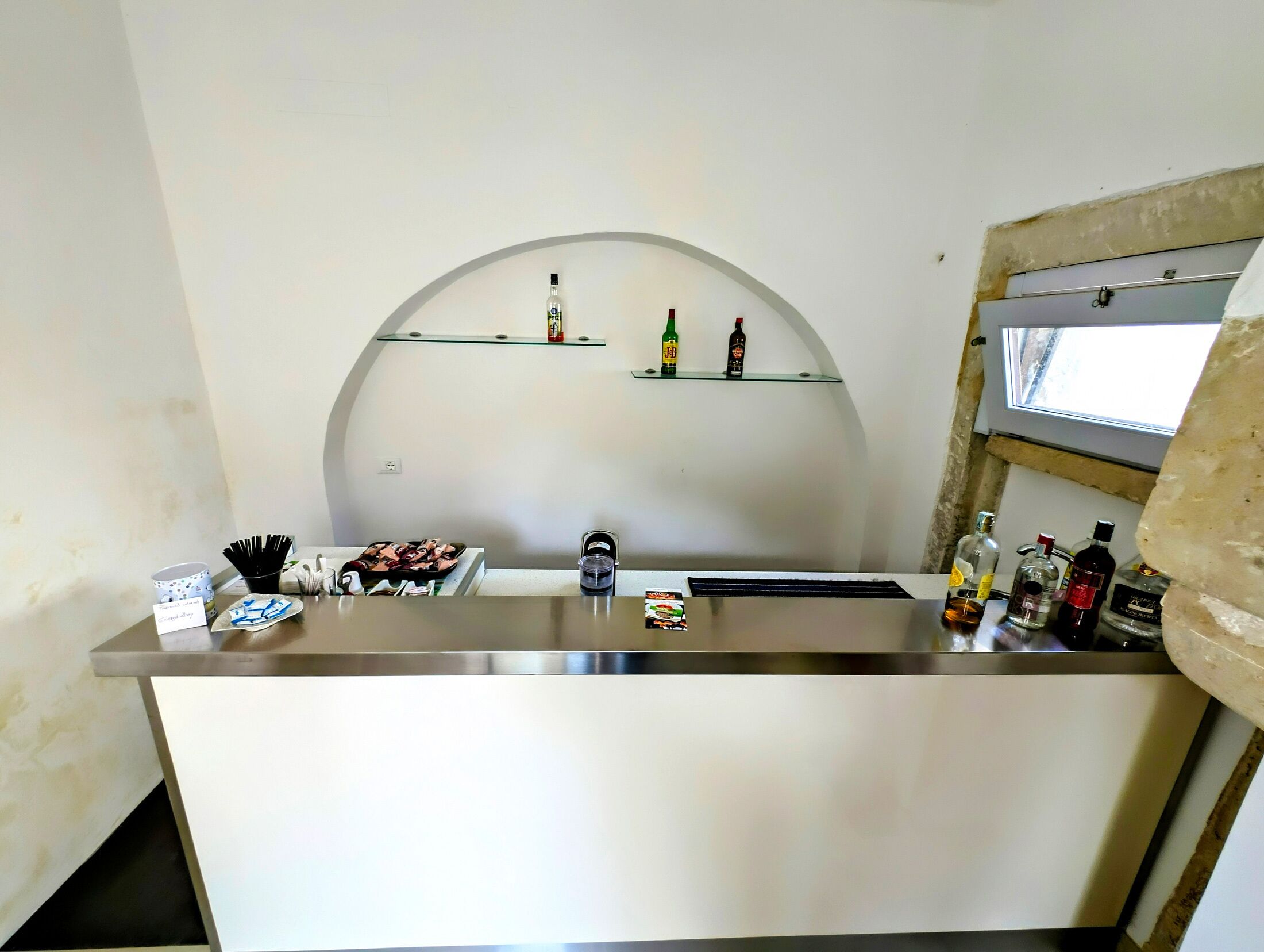 Zona de bar con mostrador, estantes con botellas y una ventana.