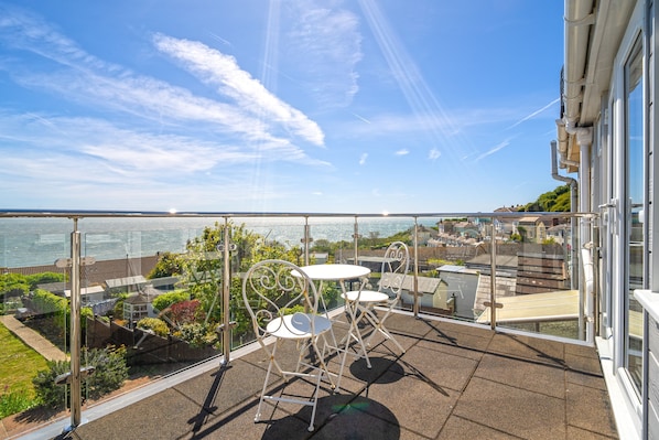A balcony with a glass railing overlooking a body of water and a residential area.