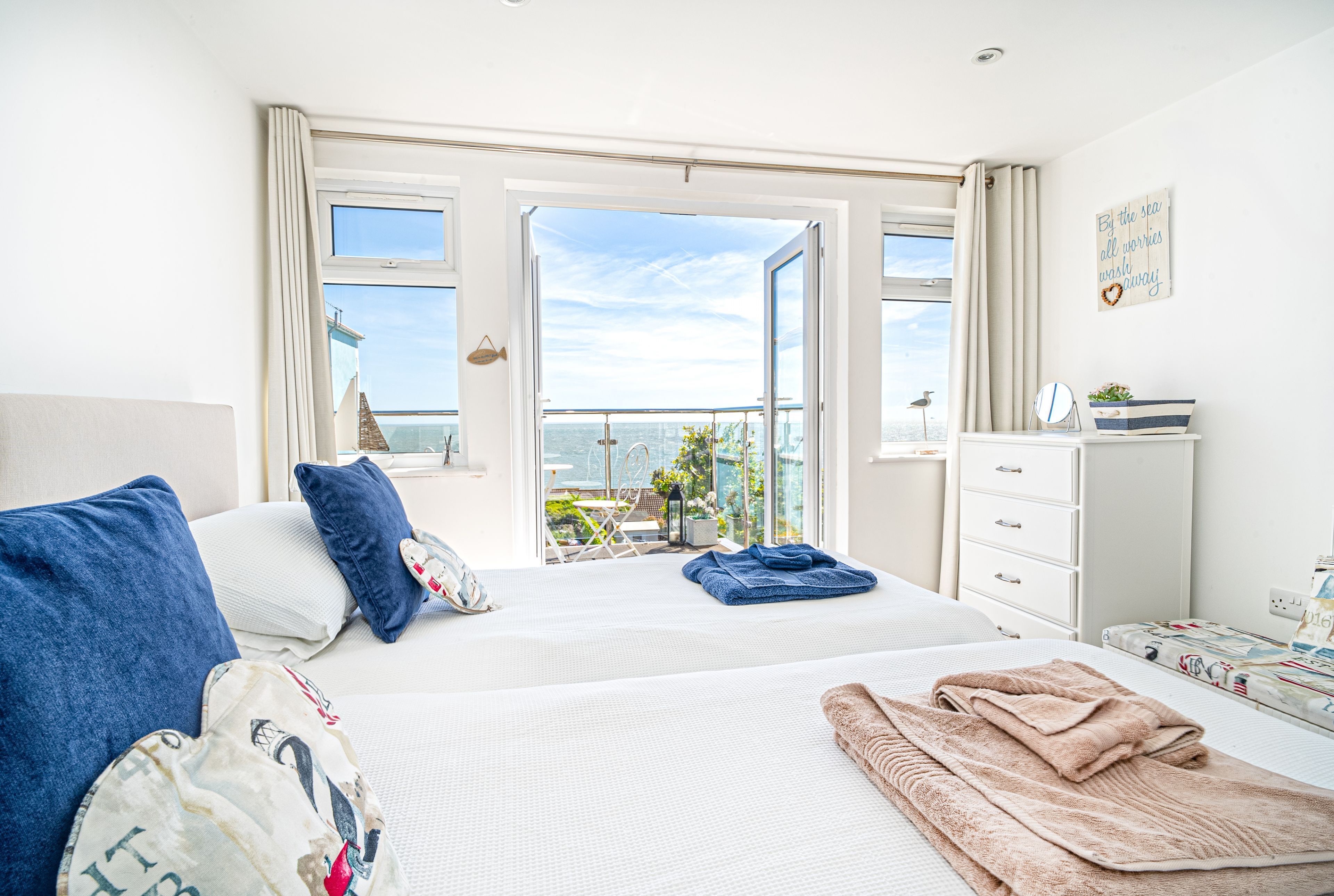 A hotel room with a bed, a dresser, a mirror, and a view of the sea.