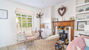 A cozy living room with a fireplace, wicker furniture, and a view of the outdoors. - Jan Dee Cottage -  a cottage that sleeps 6 guests  in 3 bedrooms (Ventnor)