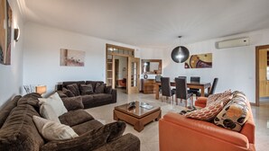Una sala de estar con un sofá marrón, un sofá naranja, una mesa de centro y un comedor con una mesa y sillas.