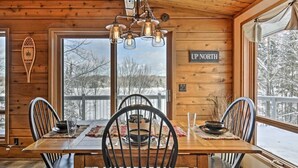 Un interior de fusta amb taula de dinar preparada per a quatre, un penjador i vista a un paisatge nevat a través de grans finestres.