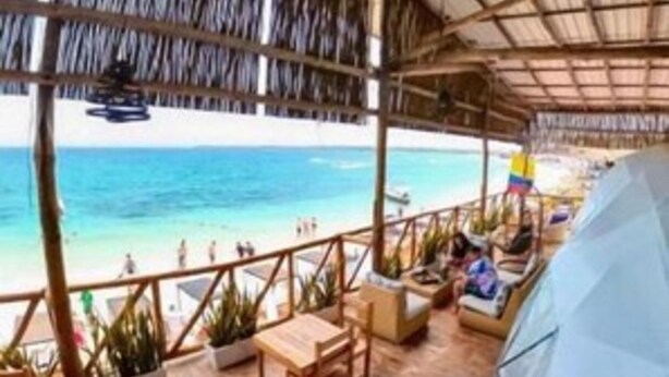 A covered outdoor area with wooden flooring, tables, chairs, and potted plants. - Cabana Glamping Geronimo  (Cartagena)