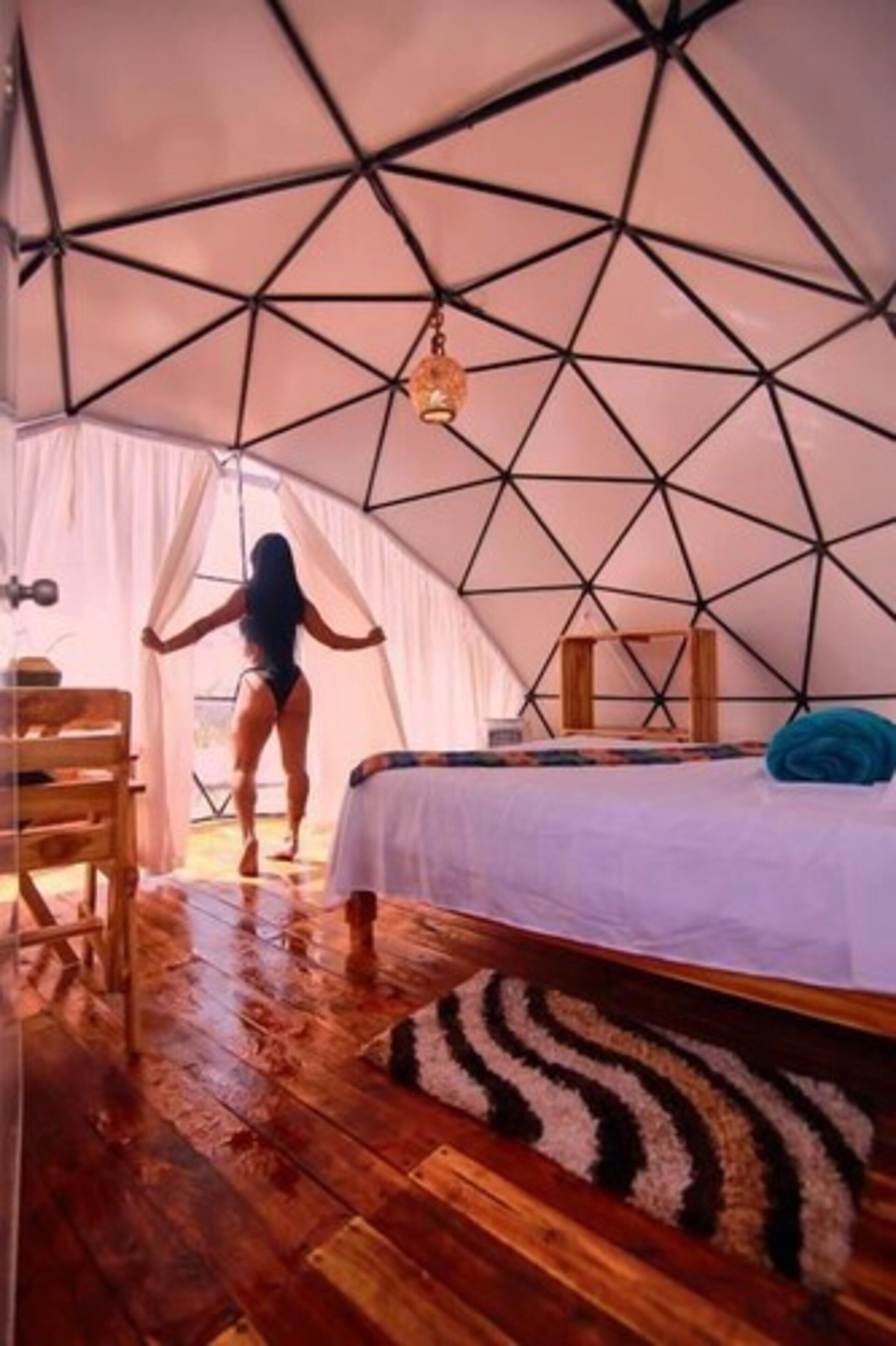 A tent with a geometric ceiling design, a bed with a white sheet, a zebra-patterned rug, and a wooden chair.