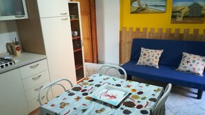 A small kitchen with a gas stove, a dining table with a fruit and vegetable tablecloth, a blue sofa with patterned cushions, and a wall with two paintings. - we think of the holidays (VILLASIMIUS)