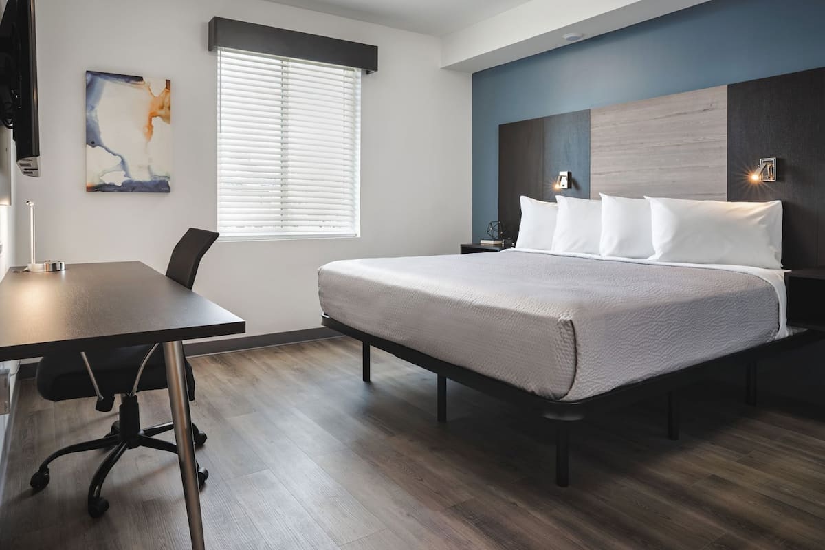 Een moderne hotelkamer met een groot bed, een bureau en een raam met zonwering.