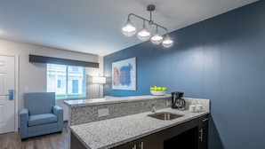 A modern kitchen with a granite countertop, dark cabinetry, and a blue accent wall. - Stay APT Suites Alexandria-Fort Belvoir (Alexandria)