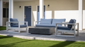 A covered outdoor seating area with two sofas and two chairs, a concrete table, and a door with an exit sign. - Stay APT Suites Alexandria-Fort Belvoir (Alexandria)