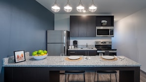 A modern kitchen with granite countertops, stainless steel appliances, and a central island with bar stools. - Stay APT Suites Alexandria-Fort Belvoir (Alexandria)