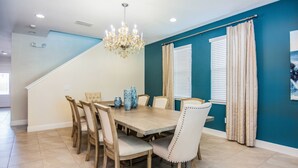 A dining room with a wooden table, six chairs, a chandelier, and teal walls. - Gorgeous Single Home with Private Pool at Encore (Kissimmee)