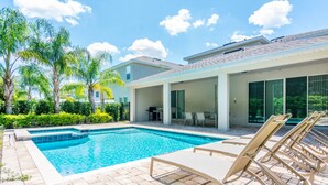 A swimming pool with lounge chairs, a covered patio area, and a view of a residential building. - Gorgeous Single Home with Private Pool at Encore (Kissimmee)