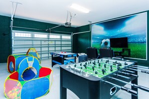 Um quarto com mesa de futebol, televisão de tela grande e área de recreação com piscina de bolinhas e estrutura de escalada.