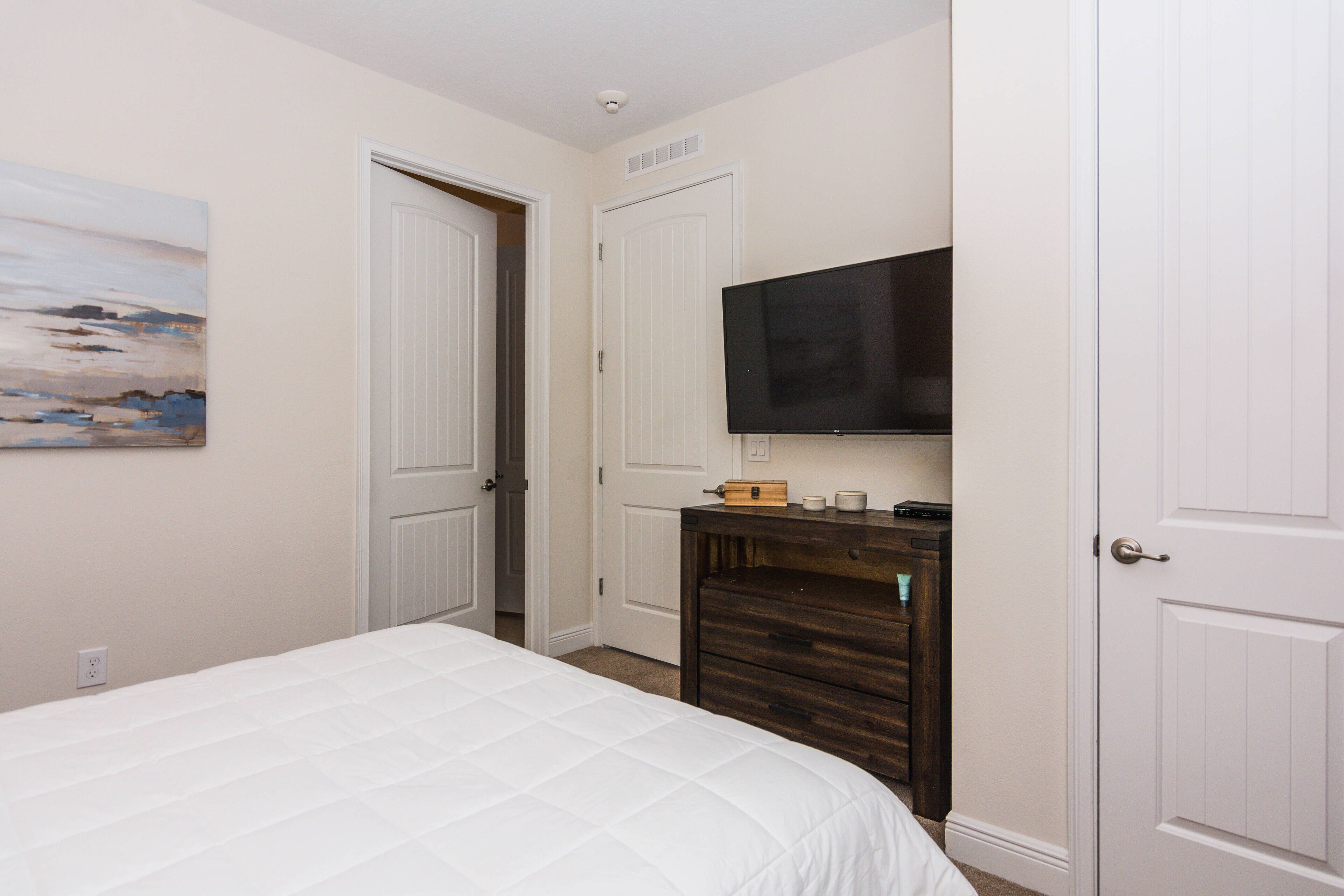 Un dormitorio con cama, televisor montado en la pared y puerta que da a otra habitación.