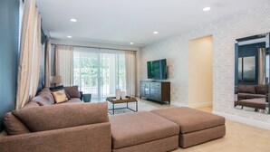 A modern living room with a sectional sofa, a TV mounted on the wall, and a large window with curtains. - Gorgeous Single Home with Private Pool at Encore (Kissimmee)