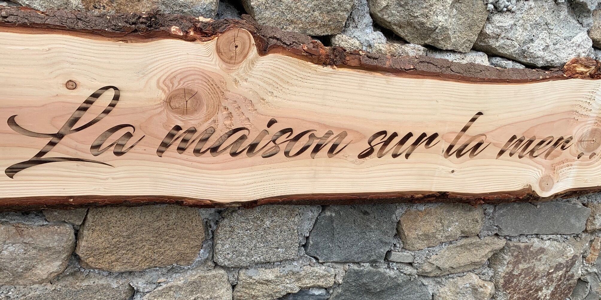 A wooden sign with carved text against a stone wall.