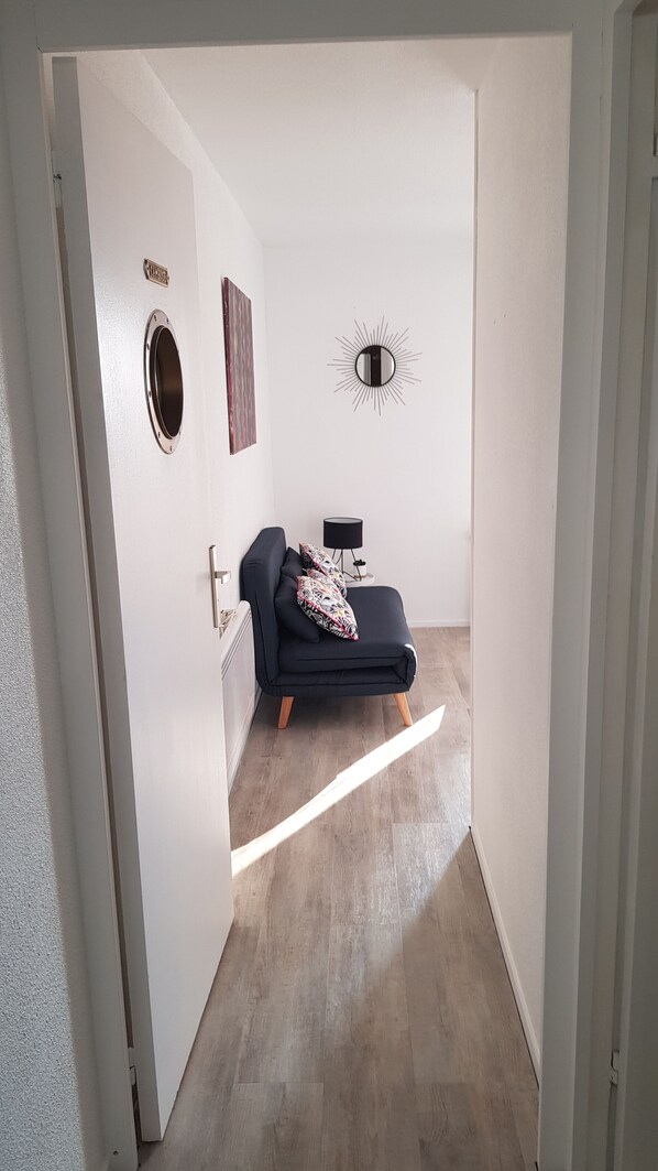 A room with a dark blue sofa, a round mirror, a small table with a lamp, and a wall-mounted sunburst decoration.