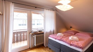 Un dormitorio con cama, radiador, ventana con cortinas y balcón.