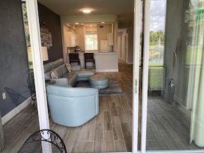 Relax in a spacious living area with a sofa, ottoman, and dining table, offering a view of lush greenery through the glass door.