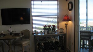 Un comedor con una mesa lista para dos personas, un televisor montado en la pared y una ventana con persianas.