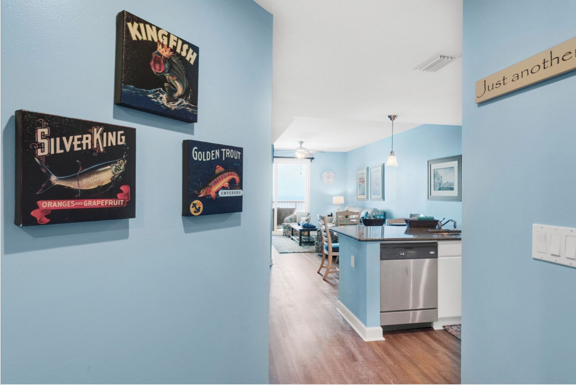 A kitchen with a dishwasher, a dining area with a table and chairs, and a hallway with a ceiling fan.