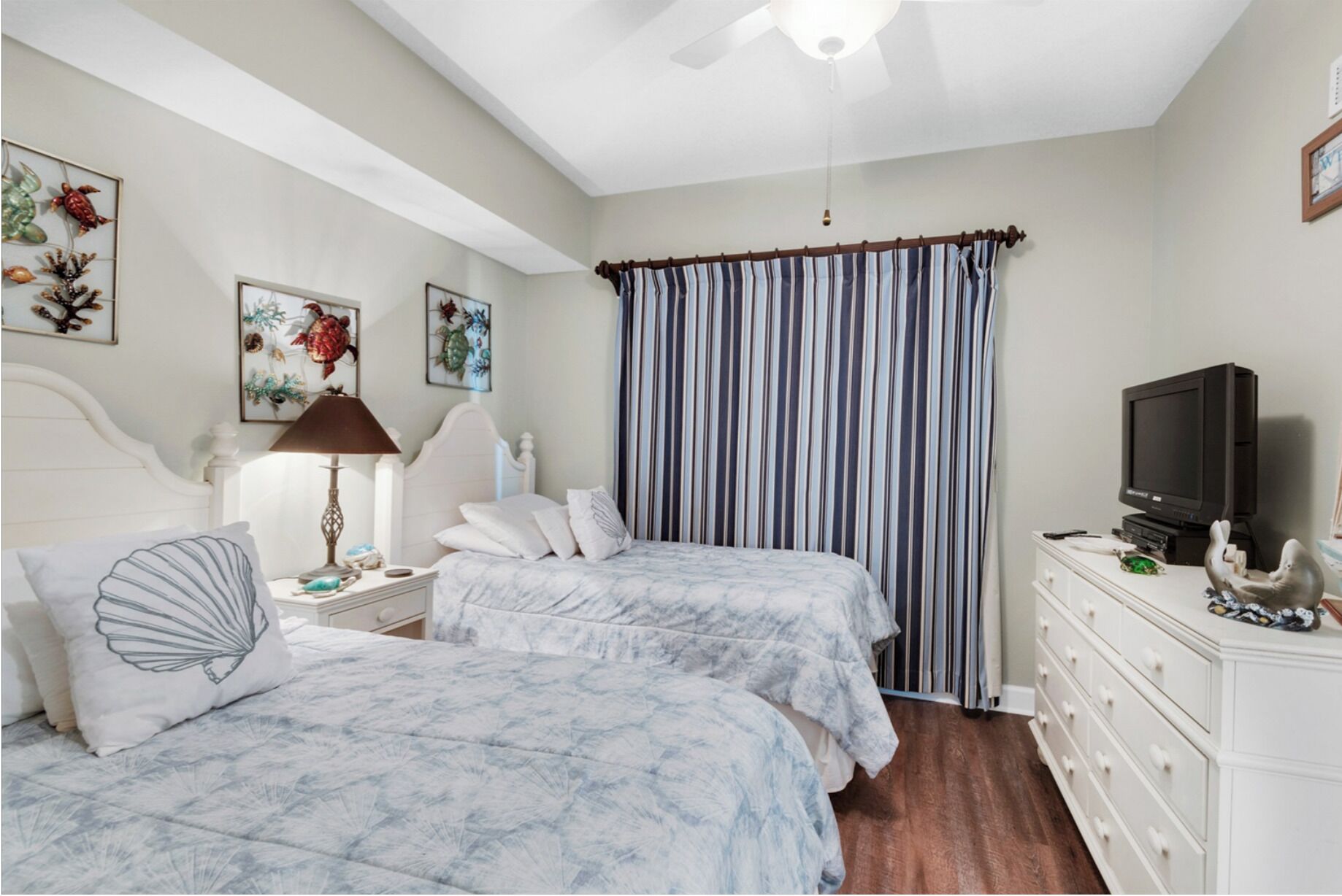 A bedroom with two beds, a ceiling fan, a television, and artwork on the walls.