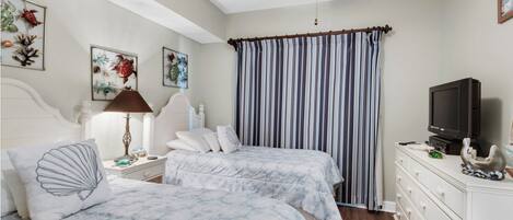 A bedroom with two beds, a ceiling fan, a television, and artwork on the walls.