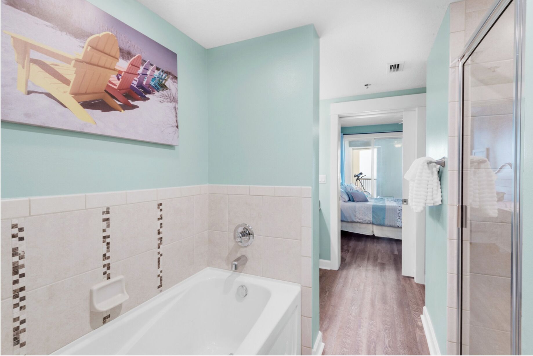 Een badkamer met een badkuip, een douche en een glazen deur naar een slaapkamer.