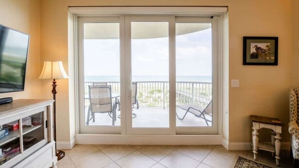 Una stanza con televisione, una lampada, e una porta scorrevole in vetro che dà su un balcone con sedie e un tavolo.