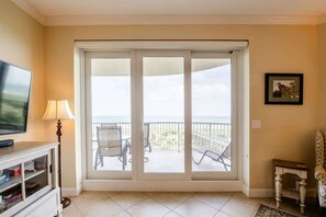 Ein Zimmer mit Fernseher, Lampe und einer Schiebetür zu einem Balkon mit Stühlen und Tisch.