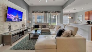 Een moderne woonkamer met een grote flatscreen televisie, een plafondventilator en een bank.