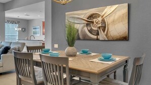 Een eethoek met een houten tafel, grijze stoelen en een blauwe vaas met groene planten.
