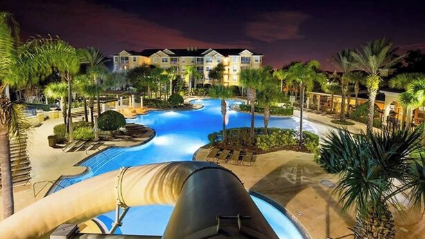 Een resort met een groot zwembad, palmbomen en een gebouw met meerdere balkons.