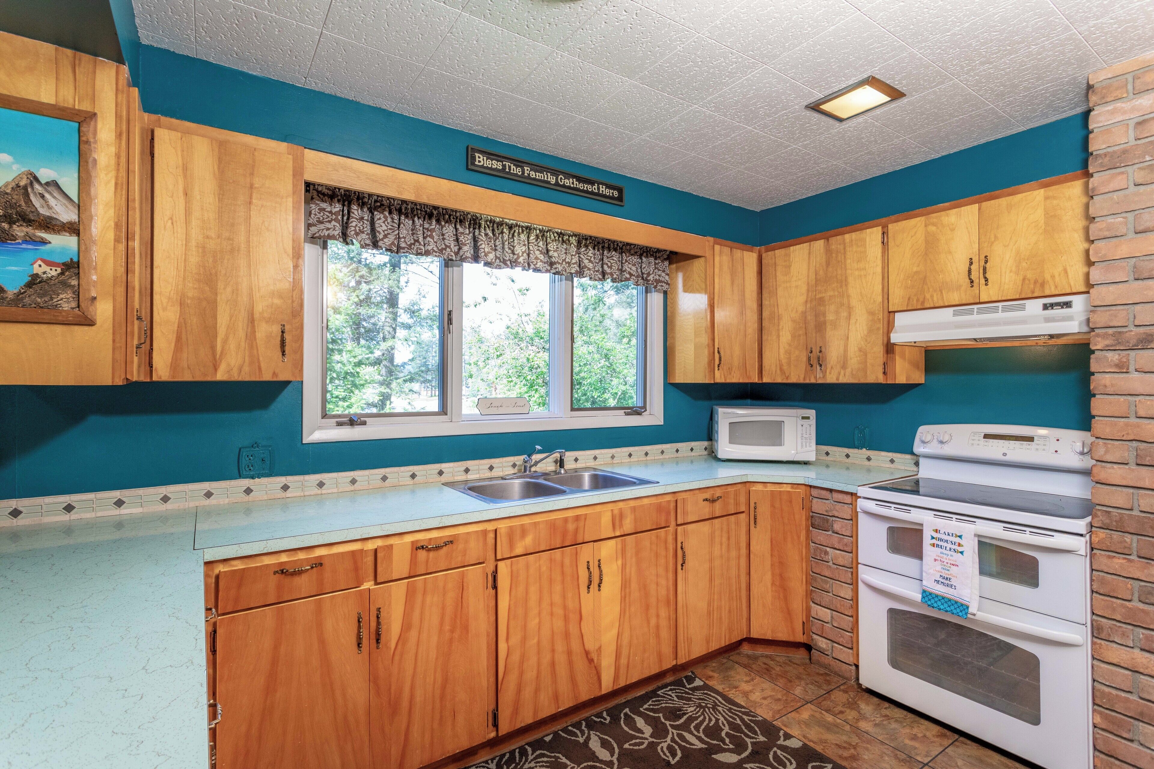 A kitchen with wooden cabinets, a microwave, a stove, and a window with a view of trees.