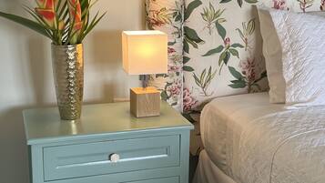 Un dormitorio con cabecera estampada con motivos florales, una mesita de noche con lámpara y una planta decorativa.