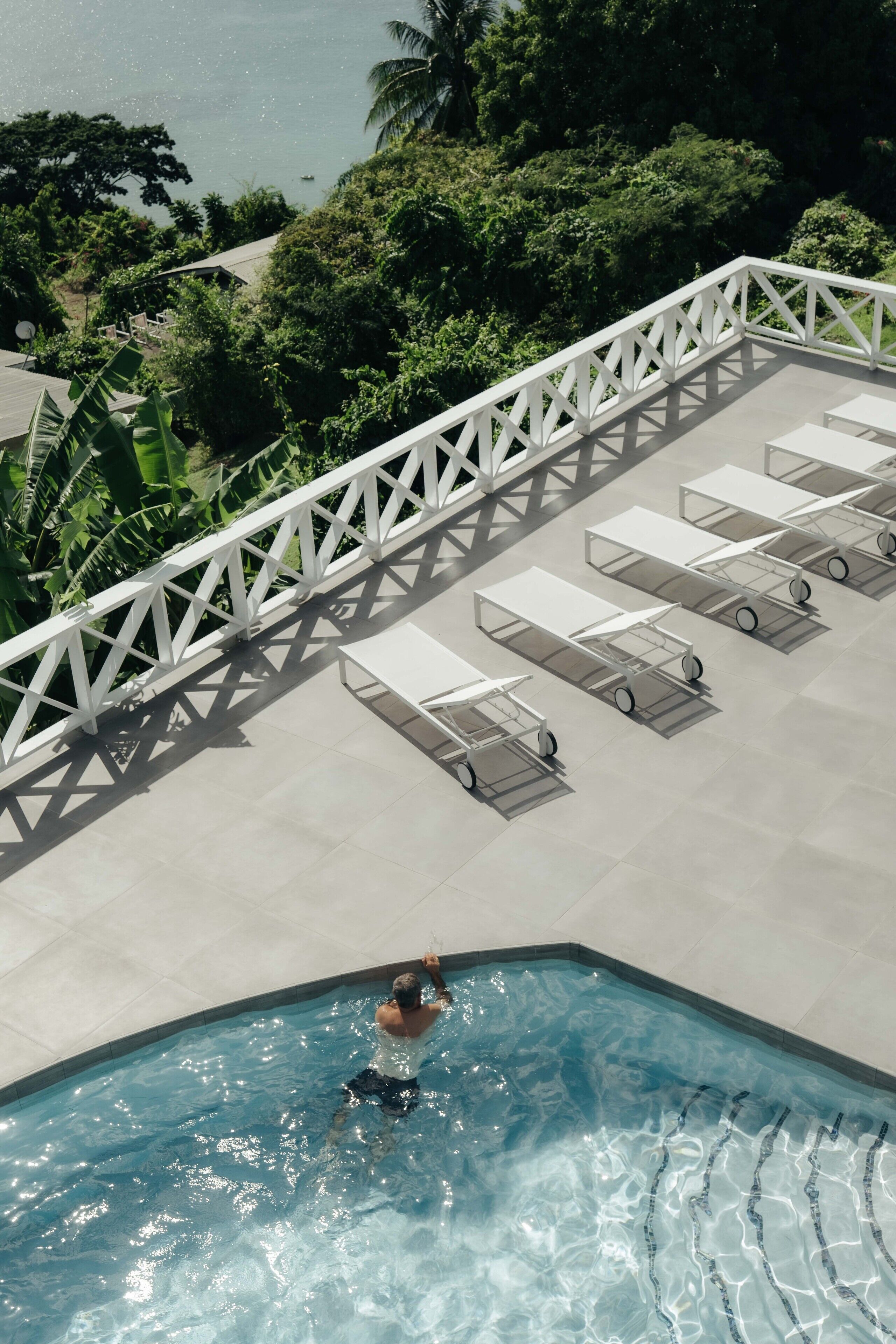 Zona de piscina con barandilla blanca, sillas de descanso y una persona nadando.