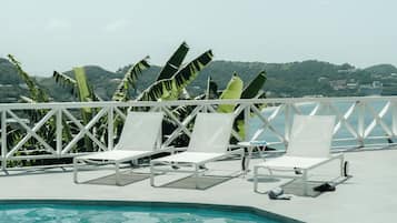 Zona de piscina con sillas reclinables blancas y vista al paisaje.