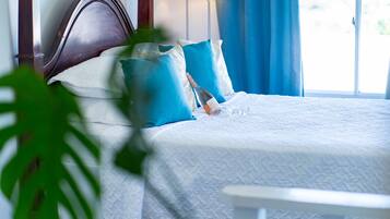 Una cama bien hecha con un edredón blanco, dos almohadas azules y un cabecero de madera.
