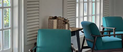 A room with teal chairs, a woven ottoman, and a table with a basket.
