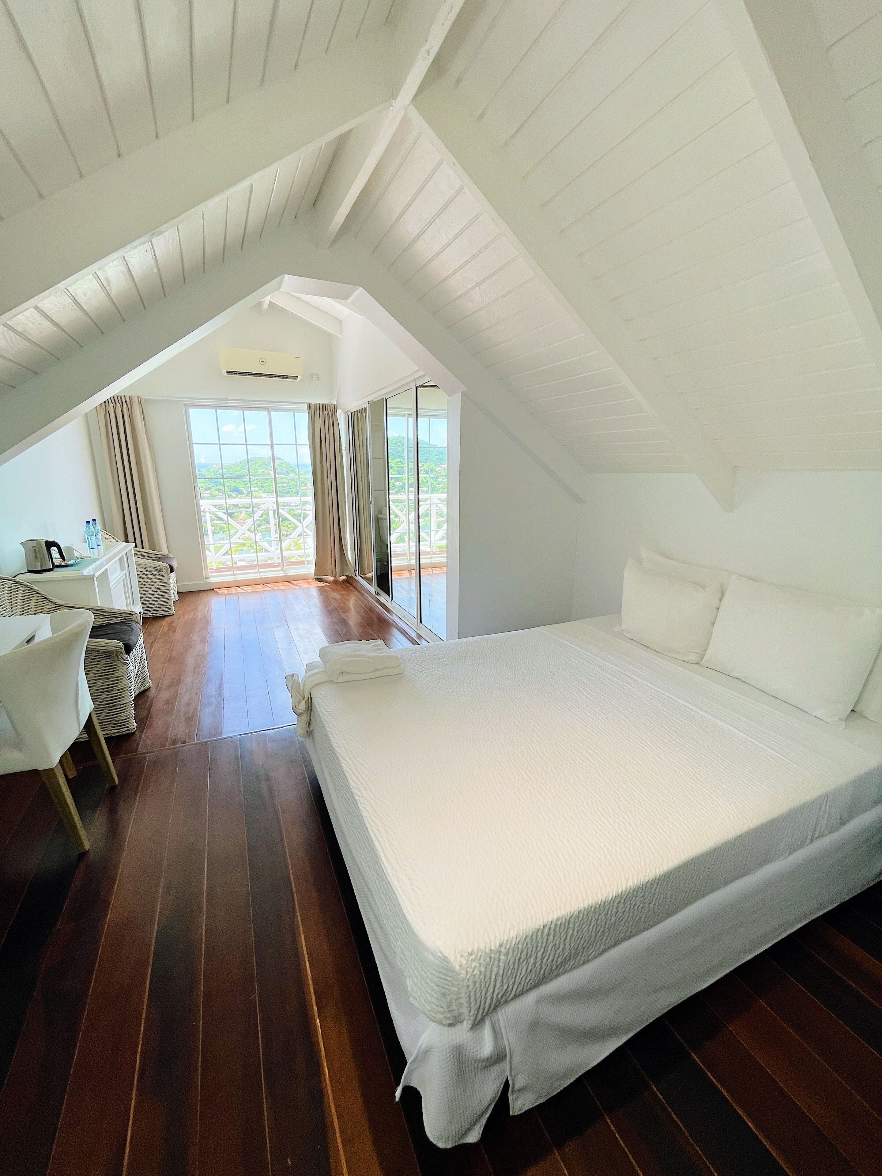 Un dormitorio con una cama grande, un escritorio y una silla, con vista a la vegetación a través de un ventanal amplio.