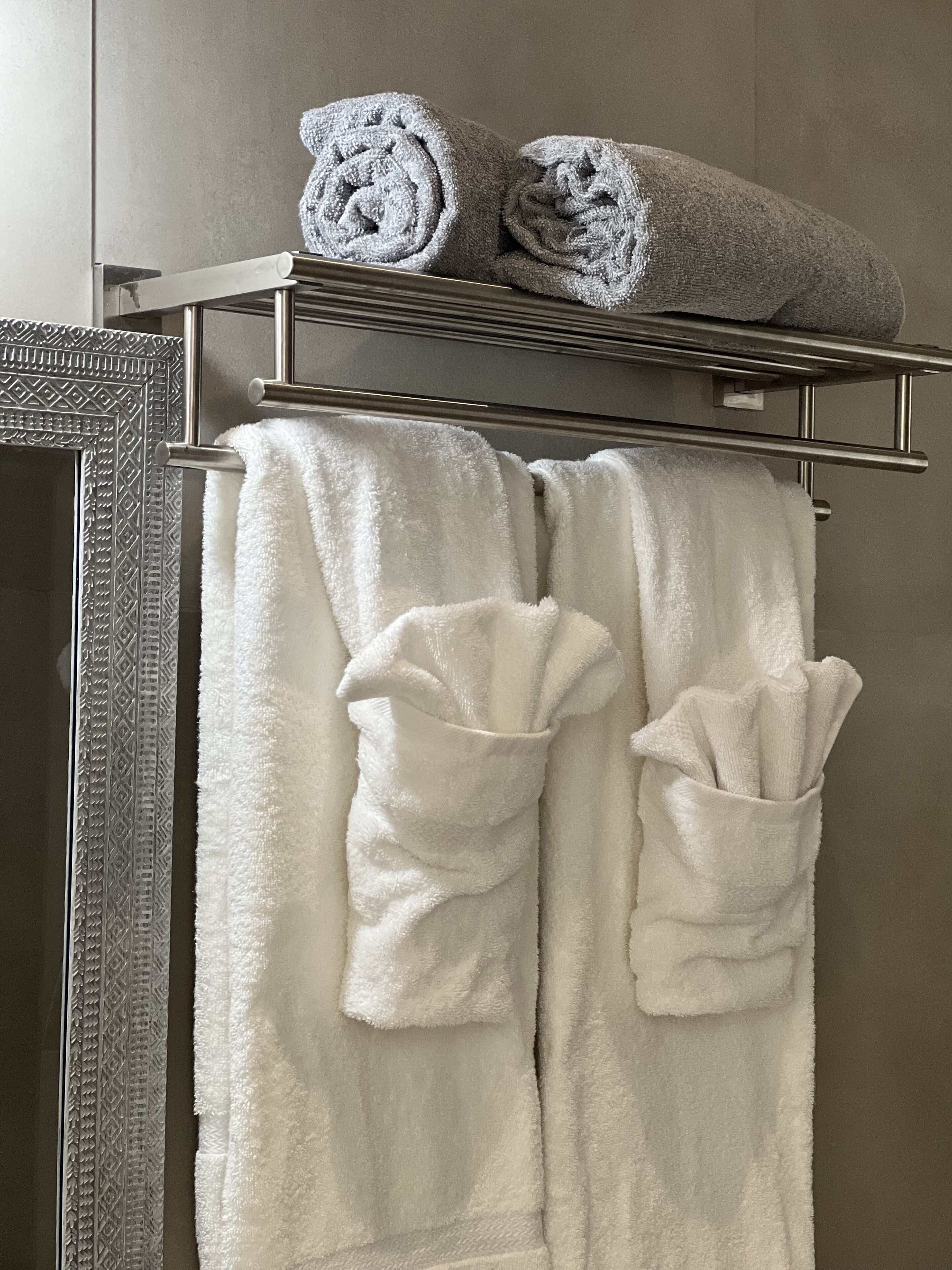 A bathroom with a towel rack holding two white towels and two rolled towels.