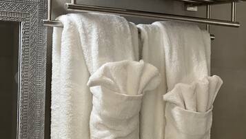 A bathroom with a towel rack holding two white towels and two rolled towels.