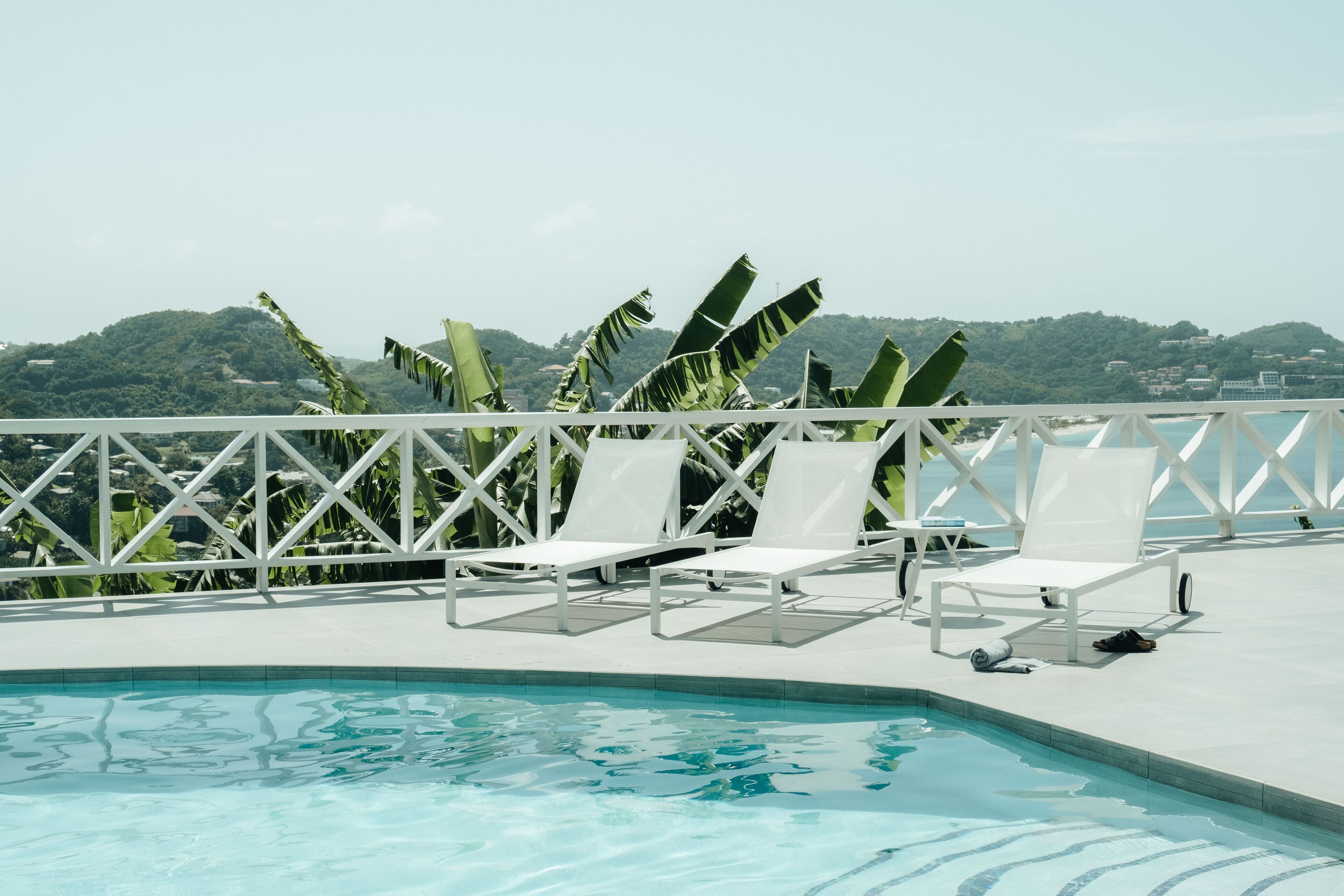 A poolside area with white lounge chairs and a view of a mountainous landscape.