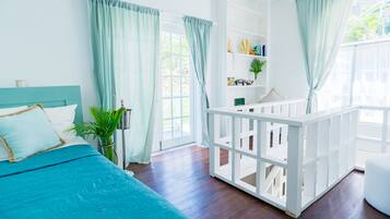 A bright bedroom with a teal bedspread, white curtains, and a white crib.