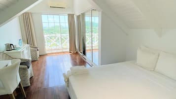 A bedroom with a large bed, a desk with chairs, and a view of greenery through large windows.