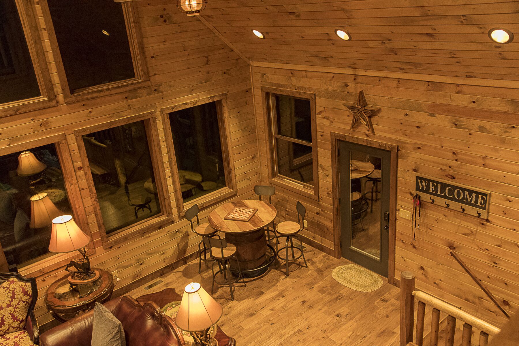 L’intérieur d’un chalet en bois chaleureux et accueillant, avec une table ronde et des chaises, un canapé en cuir et une pancarte de bienvenue.