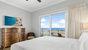 A hotel room with a large bed, a wooden dresser, a chair, a painting, and a balcony with a view of the ocean. - Sterling Breeze 203 - 1977174 (Panama City Beach)