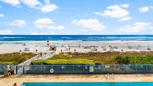 A beach with a swimming pool, a lifeguard tower, and a flag. - Sterling Breeze 203 (Panama City Beach)